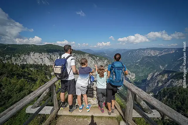 Aussichtsplattform aus Holz mit Blick ins Tal und auf die bewaldeten erge in der Ferne, Familie mit 2 Kindern im Vordergrund blicken ins Tal