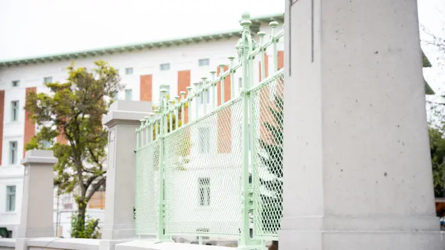 Detailansicht Zaunelement vor einem weißen Jugendstil-Gebäude mit orangenfarbenen Fensterrahmen, ein Baum steht im Vorgarten