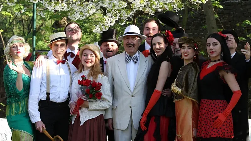 Verkleidete Personen einer Theatertruppe im Freien, unter einem blühenden Baum