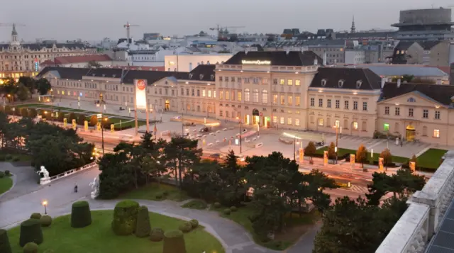 Beleuchtetes Gebäude aus der Barockzeit, Luftaufnahme, in der Abenddämmerung, im Vordergrund ein Park mit Bäumen