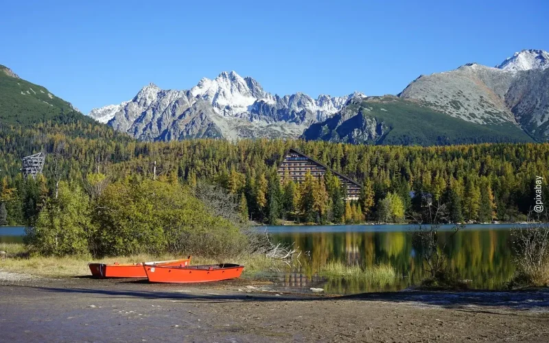 Popper See mit zwei roten Kajakbooten am Strand, im Hintergrund Hohe Tatra Gebirge mit schneebedeckten Gipfeln