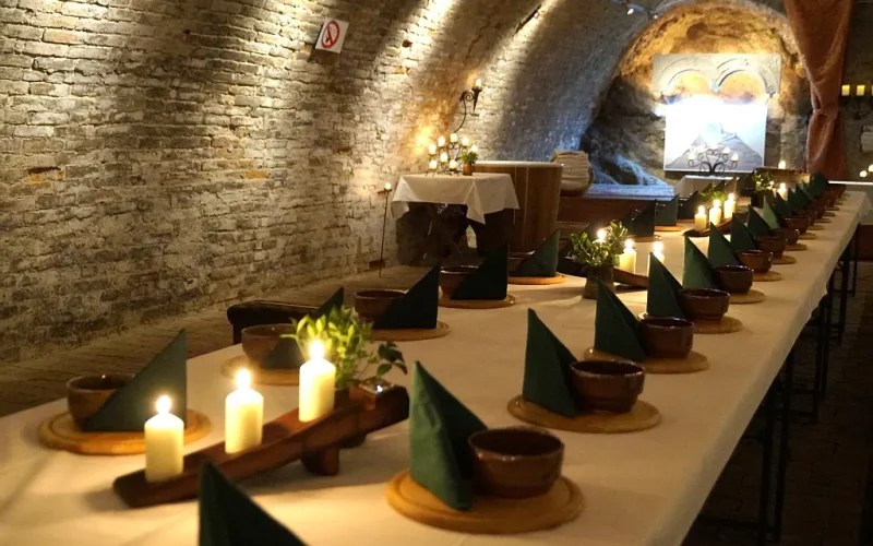 Gedeckte Tafel mit Kerzen in einem Kellergewölbe, Beleuchtung von oben