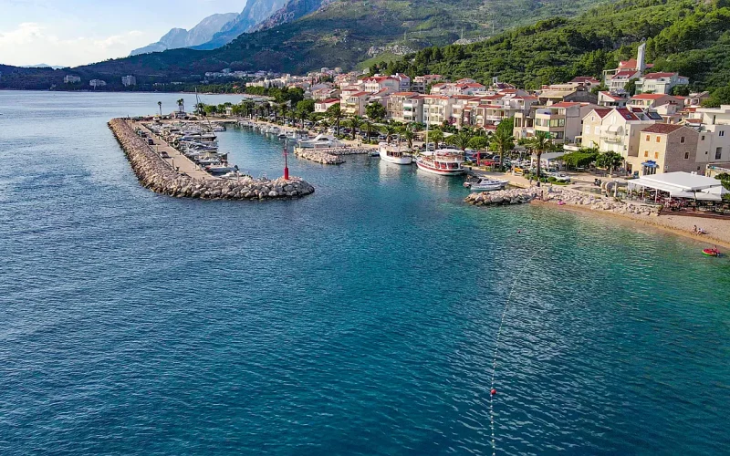 Kleine Hafenanlage vor der kroatischen Ortschaft Tucepi, im Hintergrund Berge in der Ferne, Drohnenfoto von oben