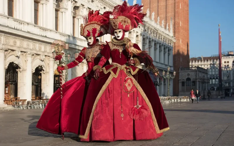 Venezianisches Maskenpaar in roter Robe auf dem Markusplatz in Venedig